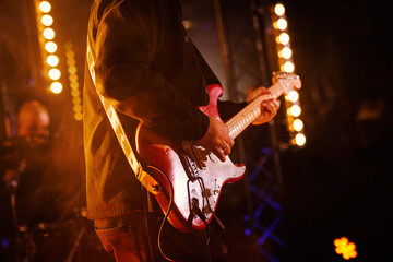 A passionate musician strums a red electric guitar on stage, illuminated by the warm glow of...