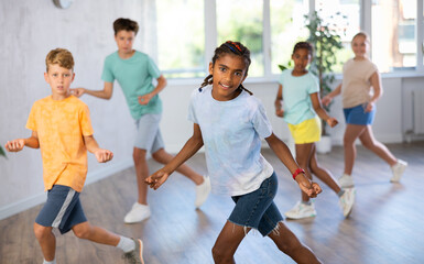 Fototapeta premium African boy performs movements during warm-up, limbering-up part of workout together with peers. Group of young girls and guys dance modern waacking in fitness club unfocused