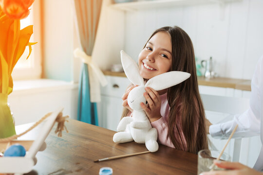 Happy Easter. Cute charming little girl in a pink dress holds a white teddy bunny isolated on a kitchen.