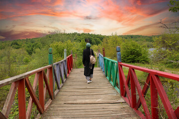 a woman walks across a bridge with a red and green railing.