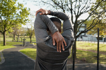 Rear view of young black man in sports clothing doing stretches in park - 762817966