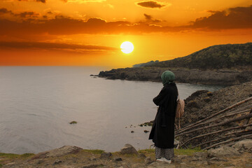 Lonely and sad girl watching sunset by the sea. Longing for the distance and the past.