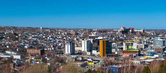 St. John's, Newfoundland, Canada - March 20, 2024: Colorful downtown St. John's with historic wooden residential buildings, commercial businesses, and a Federal Government building under a blue sky. 