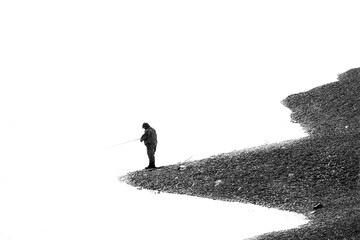 A middle aged man stands on the edge of a beach fishing in a river. The man holds a fly rod and is...