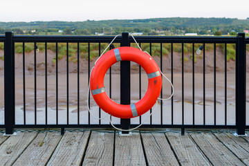 A vibrant orange polyethylene life ring hangs on a black metal railing and posts with red sand in...