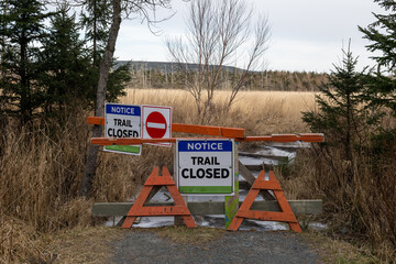 Multiple barricades across a walking trail. Signs are posted on trees and wooden barriers are...