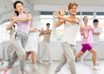 Team of positive teenagers rehearsing modern dances in dance hall