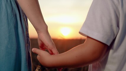 Parent taking care of child, Mom holds hand of child in park, sunset, closeup. Happy family, child holding mothers hand in sun, in nature. Family trust concept. Mom walks with kid outdoors, weekends.
