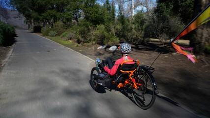 Naklejka premium Elderly senior woman riding recumbent tricycle e-bike on a path on a sunny day in a park.