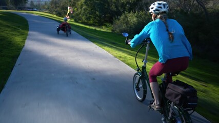 Elderly mother and mature daughter riding e-bikes on a park trail. Mother is on a recumbent electric e bike.