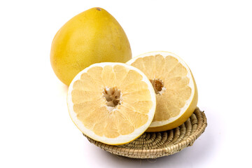 A whole pomelo grapefruit with one cut in half showing the inside segments resting in a small woven...