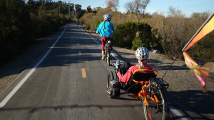 Elderly mother and mature daughter riding e-bikes on a park trail. Mother is on a recumbent...