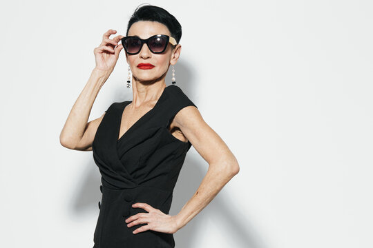 Stylish woman in black dress and sunglasses posing confidently with hands on hips for camera capture