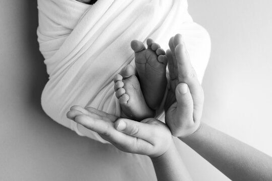 The palms of the father, the mother are holding the foot of the newborn baby. Feet of the newborn on the palms of the parents. Studio macro black and white photo of a child's toes, heels and feet.