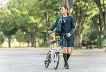 公園の中を自転車を押して歩く制服姿の中学生・高校生・女子高生
