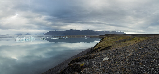 Obraz premium The shore at the edge of Jokulsarlon glacier lagoon leading towards the mountains and Vatnajokull National Park in the background 