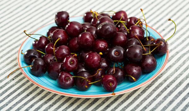 Image of fresh tasty red cherries on blue plate at table