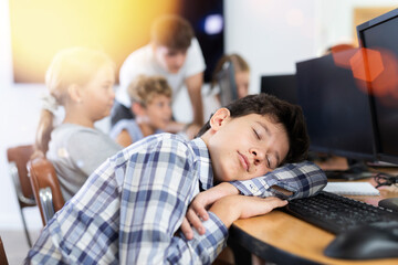 Tired preteen boy sleeping at computer table together with other attendees of IT courses