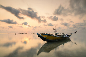 Traditional fishing boat of Andaman islands reflected in the water at sea during low tide and colorful sunset in India, Havelock island - obrazy, fototapety, plakaty