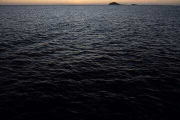 A serene twilight scene with minimal light over a calm sea and distant silhouetted islands on the...