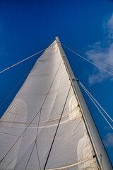 Close-up of a sailboat mast soaring into a clear blue sky, highlighting details of the sail and...