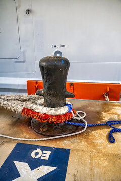 Detailed view of a ship's mooring bollard with colorful ropes and SWL label against a ship background