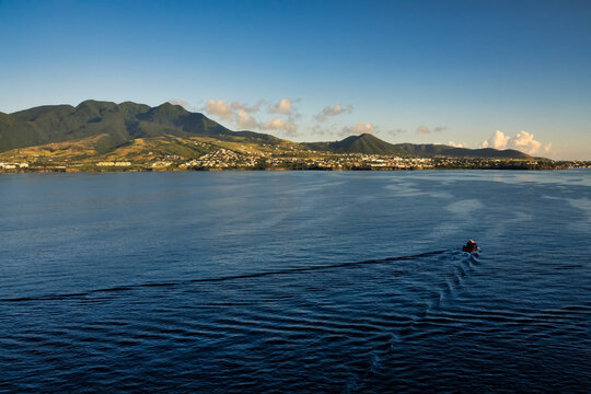 The image captures a serene seascape with green mountains in the background and a boat creating ripples in the sea