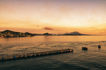 Overlooking a coastal town basking in the golden light of sunset, with calm ocean waters and silhouetted pier