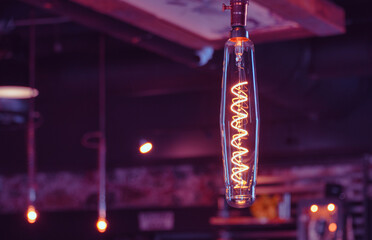 A single suspended glowing lightbulb with a filament in a vintage style setting