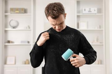 Pet shedding. Disgusted man with lint roller removing dog's hair from sweater at home