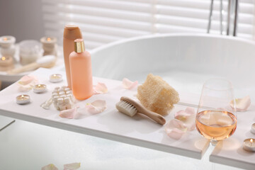Obraz na płótnie Canvas Wooden tray with wine, toiletries and flower petals on bathtub in bathroom