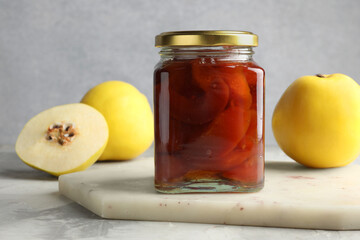 Tasty homemade quince jam in jar and fruits on grey textured table, closeup