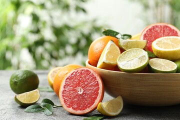 Different fresh citrus fruits and leaves on grey table against blurred background, closeup