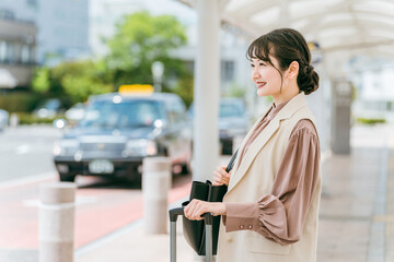 出張・旅行で駅・空港でバス・タクシーを待つ若いアジア人ビジネスウーマン（待ち合わせ）
