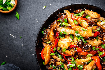 Hot stir fry chicken  slices with red paprika, mushrooms, chives and sesame seeds in frying pan. Black table background, top view - obrazy, fototapety, plakaty