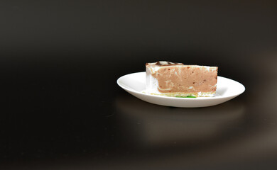 White ceramic plate with a slice of cream cheesecake with mint leaves on a black background.