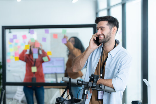 Portrait of smiling businessman talking on mobile phone while colleague using scooter in office