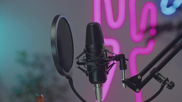 Close-up view of condenser microphone with pop filter in recording studio with multicolored neon light