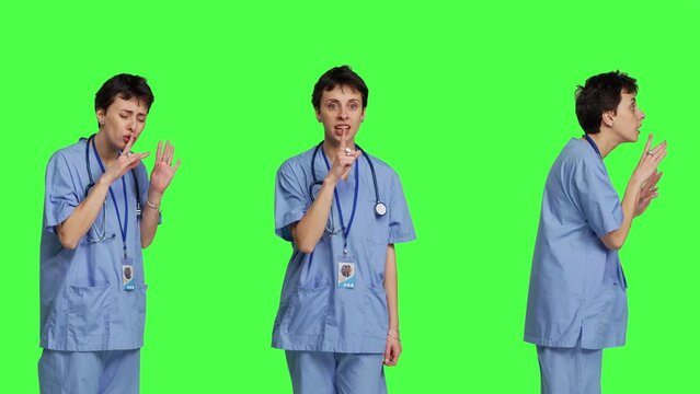 Medical assistant asking to keep quiet and be silent against greenscreen, showing hush mute symbol to keep privacy and silence. Young nurse showing secrecy taboo sign. Camera B.