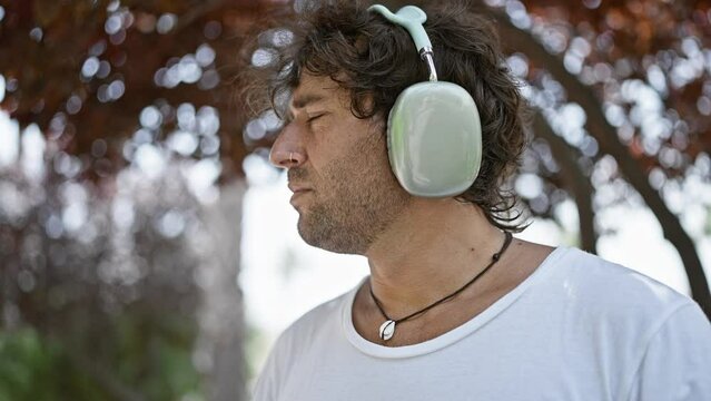 Pensive hispanic man wearing headphones outdoors in an urban setting, depicting a moment of leisure or contemplation.