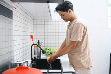 Asian man washing lemon with water in sink at kitchen