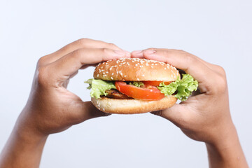 Hand holding delicious burger with beef patty, tomato and lettuce on white background, closeup