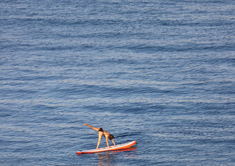 A young girl doing a cartwheel on top of a paddle board in the bay water.