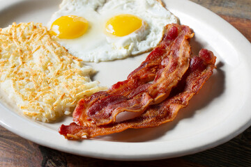 A closeup view of a breakfast plate featuring fried eggs, hash browns, and bacon.
