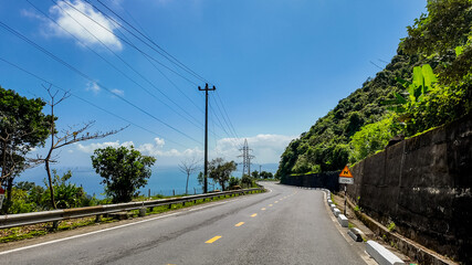 Scenic coastal road with lush greenery, clear blue sky and ocean view, perfect for travel and...