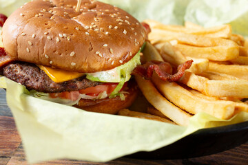 A closeup view of a bacon avocado cheeseburger, with french fries.