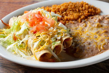 A view of a combo plate with three taquitos, rice and beans.