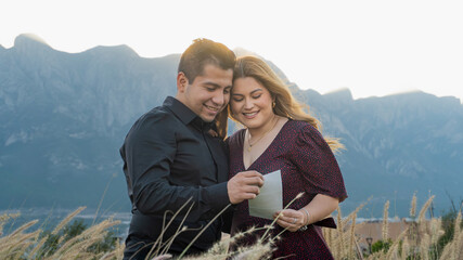 Obraz premium young hispanic couple smiling holding ultrasound, hill background, looking at ultrasound
