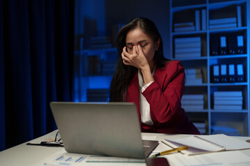 Asian businesswoman is tired, headache, sleepy and bored from sitting at a desk for a long time working on a laptop computer. Problematic financial paperwork Office syndrome concept.