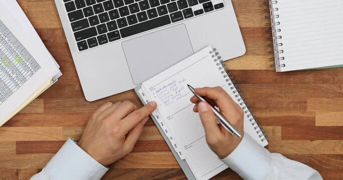 Office employee marks completed assignments with pen in pad